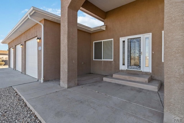 entrance to property featuring an attached garage and stucco siding