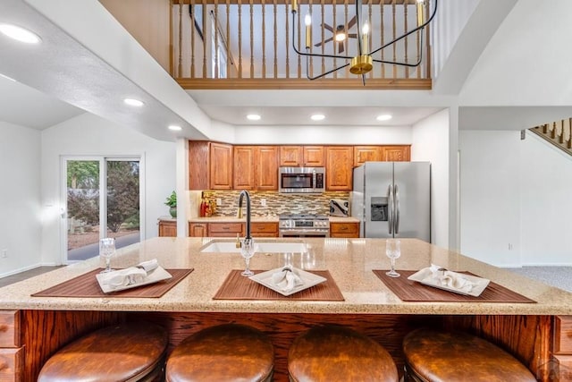 562 Brookeway, Florence, CO 81226 - kitchen featuring stainless steel appliances, a high ceiling, brown cabinets, light stone counters, and decorative backsplash