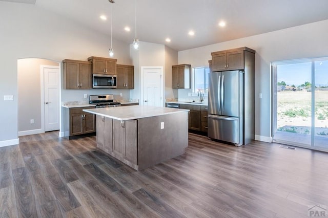 kitchen with a center island, arched walkways, stainless steel appliances, light countertops, and hanging light fixtures