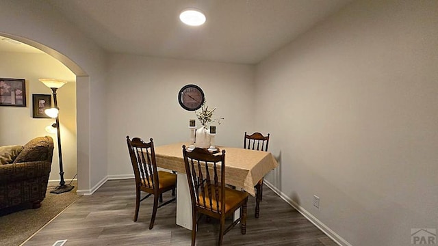 dining space featuring baseboards, arched walkways, and dark wood-style flooring