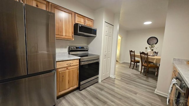 kitchen with light wood finished floors, baseboards, brown cabinets, stainless steel appliances, and light countertops