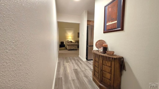 hallway featuring light wood-style floors, baseboards, and a textured wall