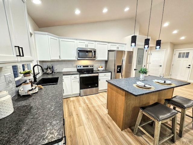 kitchen with a breakfast bar, a sink, stainless steel appliances, light wood finished floors, and vaulted ceiling