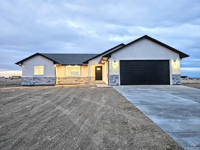 view of front of property featuring a garage, stone siding, driveway, and stucco siding