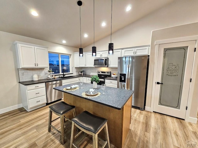 kitchen with a sink, a kitchen island, dark countertops, light wood-style floors, and appliances with stainless steel finishes