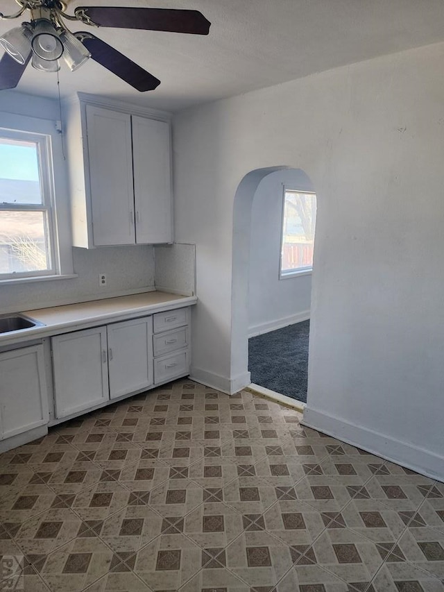 kitchen featuring arched walkways, light countertops, baseboards, and white cabinetry