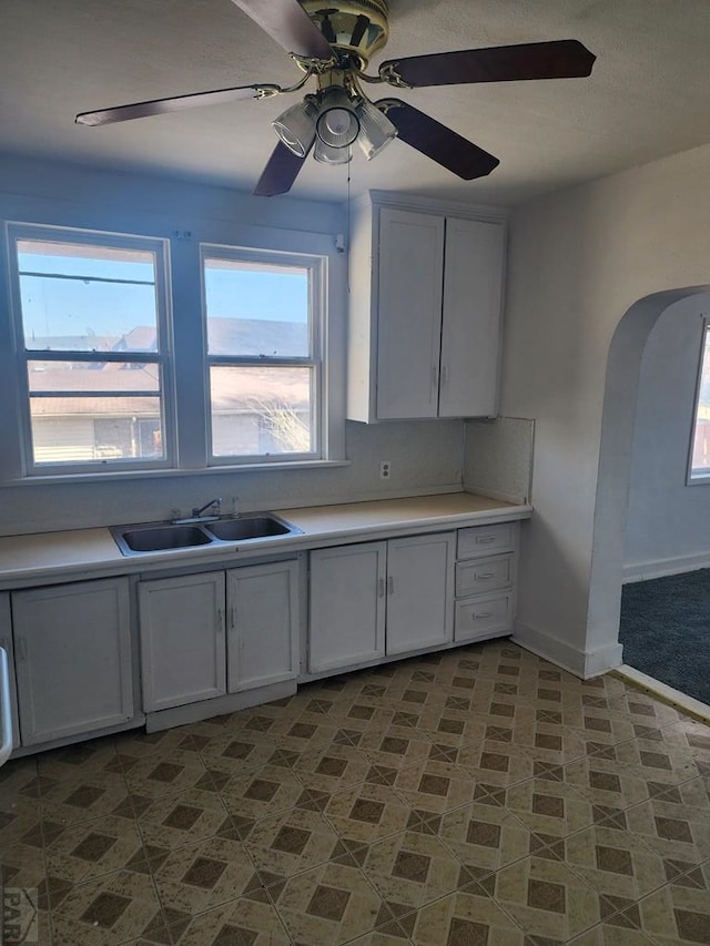 kitchen with light countertops, white cabinets, a sink, and arched walkways