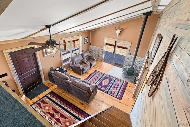 living area with a wood stove, ceiling fan, lofted ceiling with beams, and wood finished floors