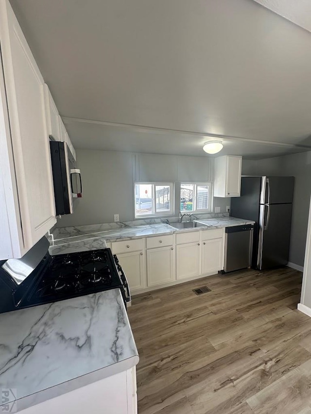 kitchen with visible vents, light wood-style flooring, stainless steel appliances, white cabinetry, and a sink