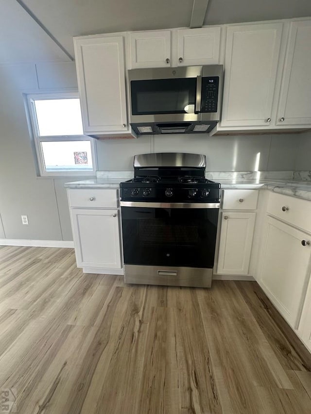 kitchen featuring black gas range, light wood finished floors, stainless steel microwave, and white cabinets