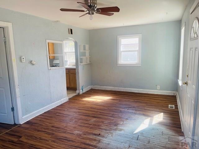 spare room with dark wood-type flooring, arched walkways, ceiling fan, and baseboards