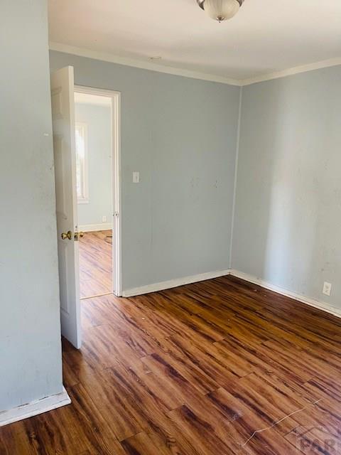 empty room with dark wood-style floors, baseboards, and ornamental molding