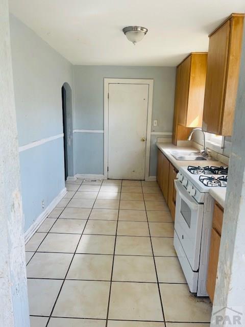 kitchen featuring arched walkways, light tile patterned floors, light countertops, white range with gas cooktop, and a sink