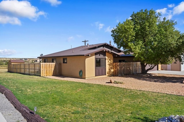 rear view of house with a yard, fence, and stucco siding