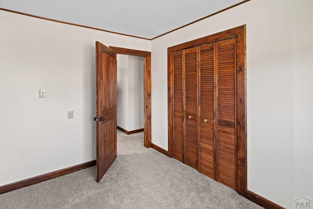 unfurnished bedroom with crown molding, baseboards, a closet, and light colored carpet