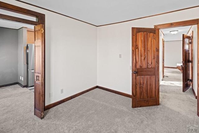 unfurnished room featuring light colored carpet, crown molding, and baseboards