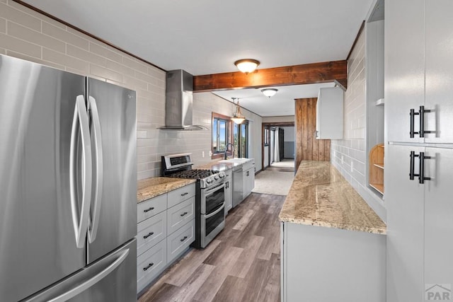 kitchen featuring decorative light fixtures, backsplash, appliances with stainless steel finishes, a sink, and wall chimney range hood