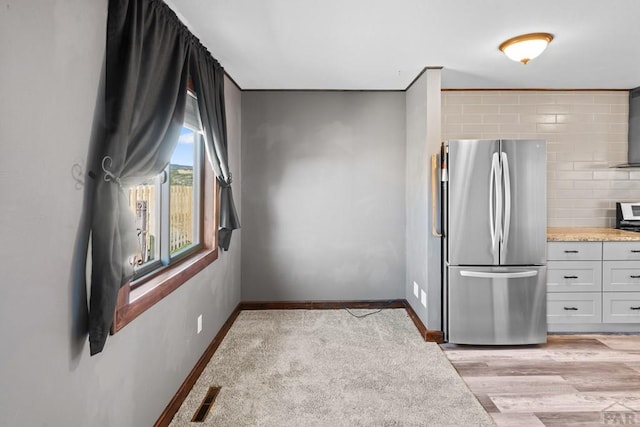 kitchen with baseboards, visible vents, decorative backsplash, freestanding refrigerator, and light countertops