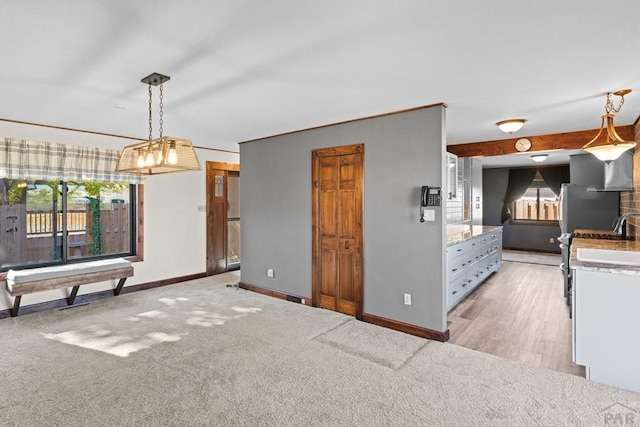 kitchen with light carpet, white cabinetry, baseboards, light countertops, and hanging light fixtures