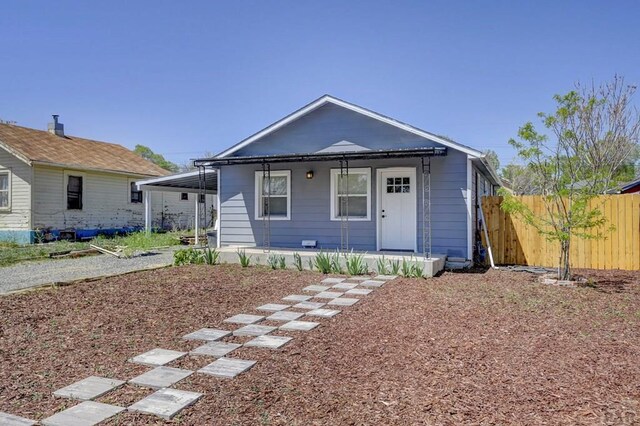 bungalow-style house featuring fence, covered porch, and a carport