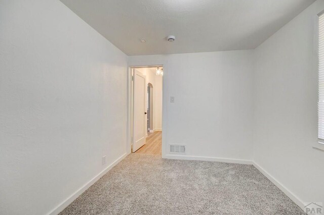 empty room with arched walkways, baseboards, light carpet, and visible vents