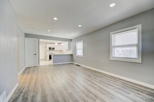 unfurnished living room with visible vents, baseboards, recessed lighting, a sink, and light wood-style flooring