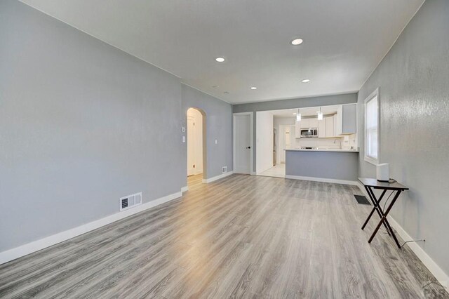 unfurnished living room featuring light wood-style floors, arched walkways, baseboards, and visible vents