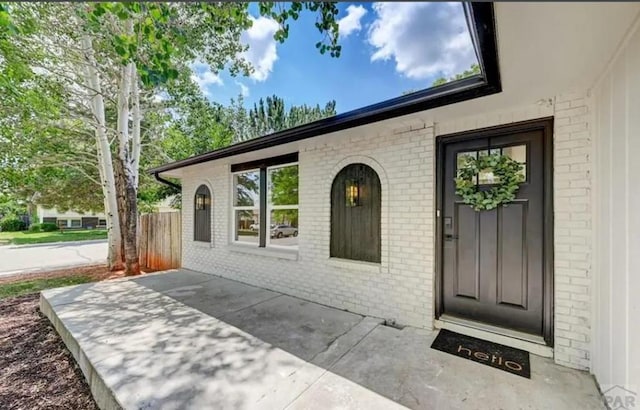 property entrance with a patio, brick siding, and fence