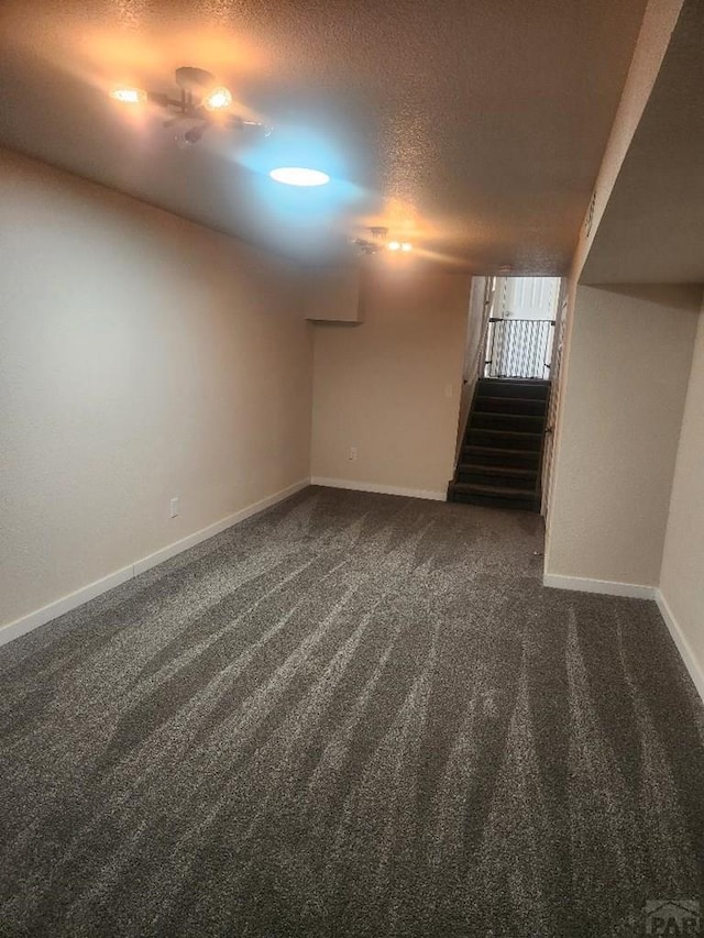 finished below grade area with a textured ceiling, dark colored carpet, stairway, and baseboards