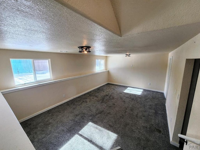 empty room featuring baseboards, dark colored carpet, and a textured ceiling