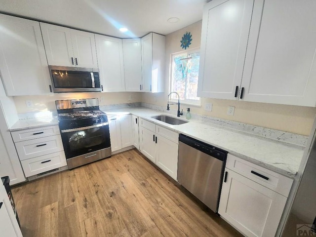 kitchen with stainless steel appliances, light wood finished floors, a sink, and white cabinetry