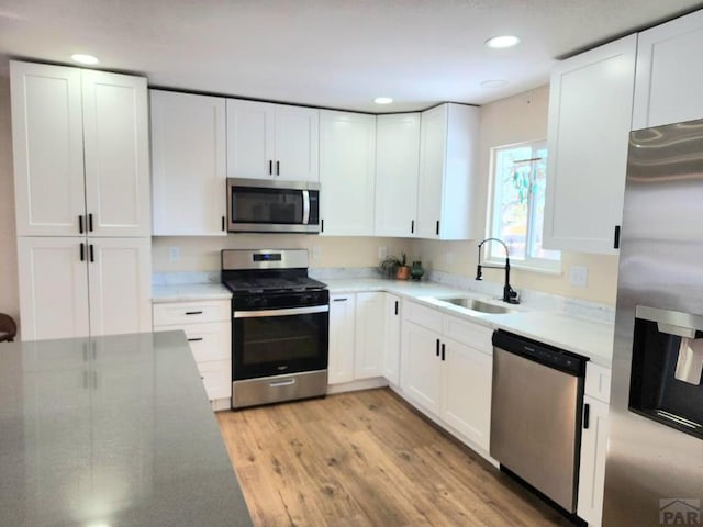 kitchen featuring light wood finished floors, appliances with stainless steel finishes, white cabinetry, a sink, and recessed lighting