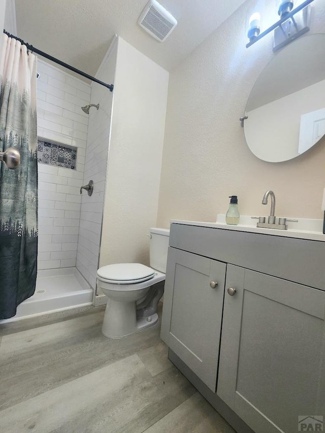 bathroom with toilet, a shower stall, visible vents, and wood finished floors