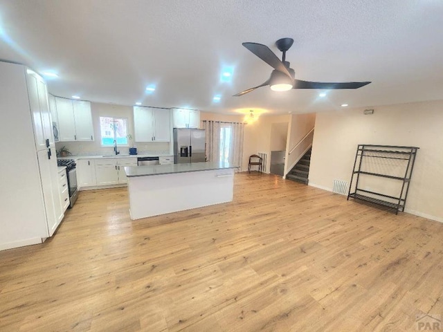 kitchen with a kitchen island, white cabinetry, light wood-style floors, open floor plan, and appliances with stainless steel finishes