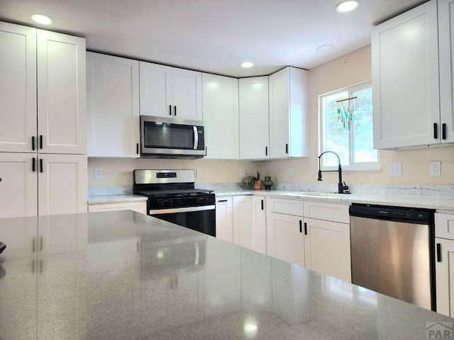 kitchen with appliances with stainless steel finishes, a sink, white cabinetry, and light stone countertops