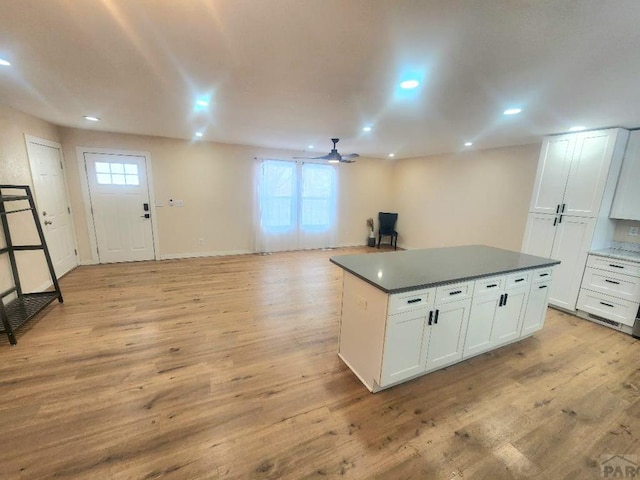 kitchen featuring white cabinets, dark countertops, open floor plan, a center island, and light wood-type flooring