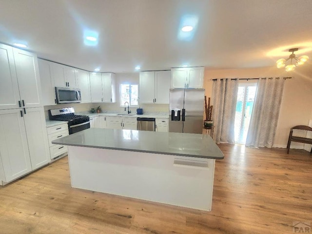 kitchen featuring a center island, light wood finished floors, appliances with stainless steel finishes, white cabinetry, and a sink