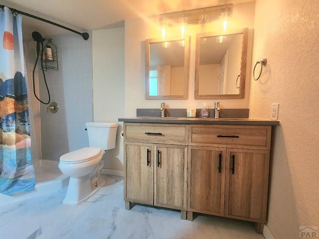 bathroom featuring toilet, a sink, marble finish floor, a tile shower, and double vanity