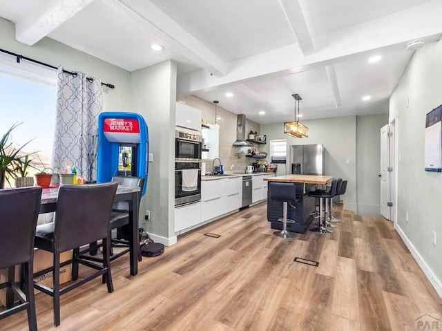 kitchen featuring a center island, light wood finished floors, appliances with stainless steel finishes, white cabinetry, and beamed ceiling