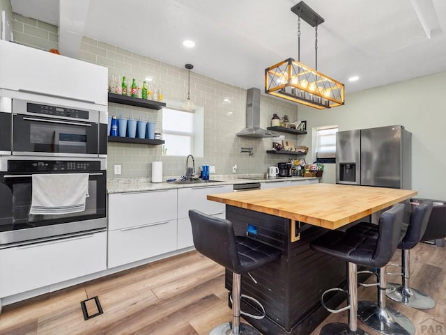 kitchen with open shelves, stainless steel appliances, a sink, wall chimney range hood, and butcher block countertops