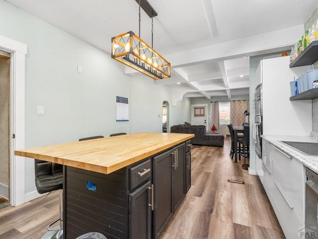 kitchen featuring arched walkways, coffered ceiling, butcher block countertops, light wood-type flooring, and open shelves