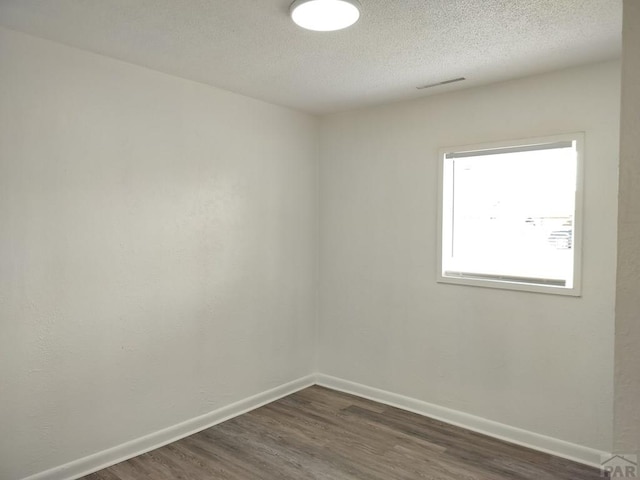 1143 25th Ln, Pueblo, CO 81006 - empty room featuring dark wood-type flooring, baseboards, and a textured ceiling