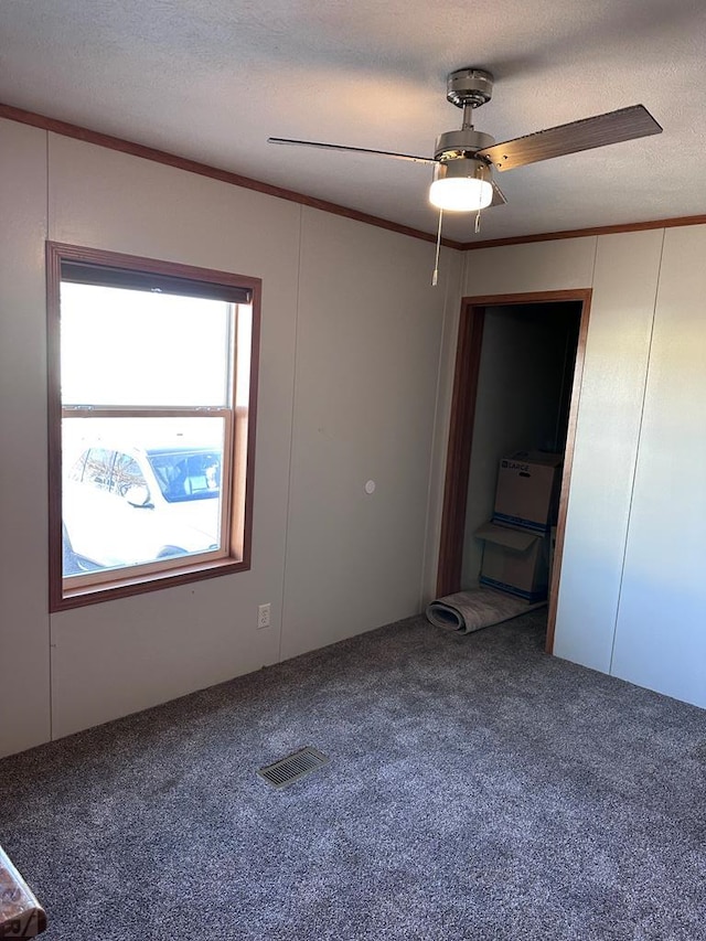 unfurnished bedroom with carpet, visible vents, ornamental molding, ceiling fan, and a textured ceiling