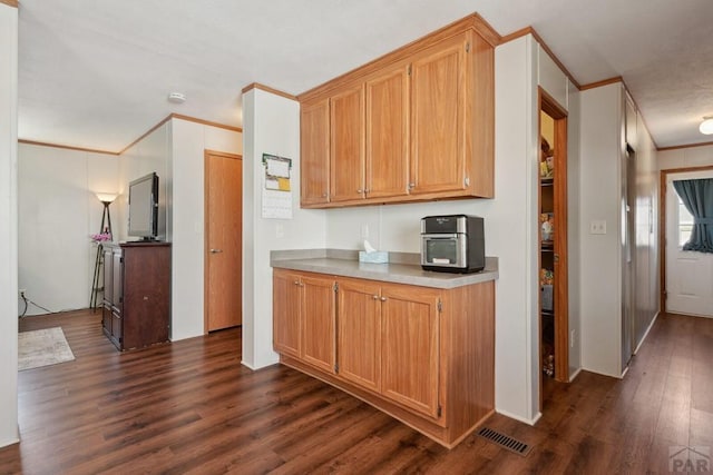 kitchen with brown cabinets, ornamental molding, light countertops, and dark wood-type flooring