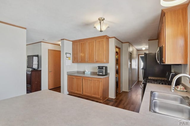 kitchen with dark wood-style floors, stainless steel microwave, ornamental molding, light countertops, and a sink