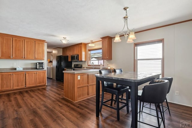 kitchen featuring dark wood-style floors, stainless steel appliances, light countertops, hanging light fixtures, and brown cabinetry