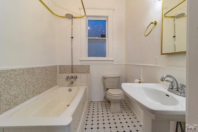 bathroom featuring toilet, a wainscoted wall, a sink, tile patterned floors, and a bathtub