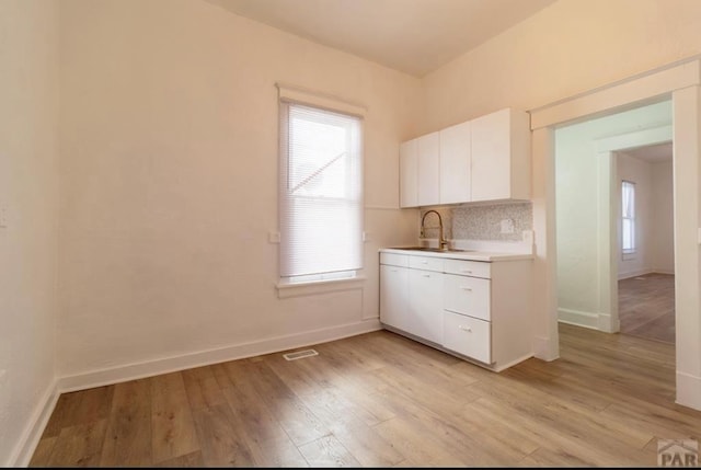 kitchen with white cabinets, a sink, light countertops, light wood-type flooring, and backsplash