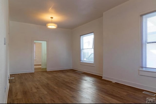 empty room featuring dark wood-style flooring, a healthy amount of sunlight, and baseboards