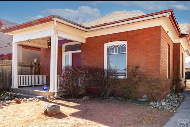 view of side of home with roof with shingles, a porch, and brick siding